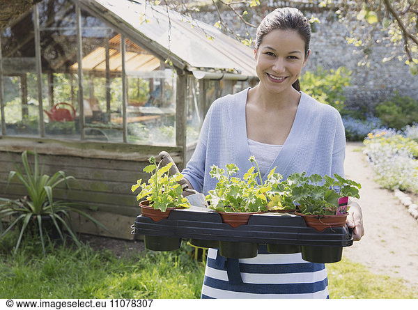 Portrait smiling woman carrying potted plants outside greenhouse garden