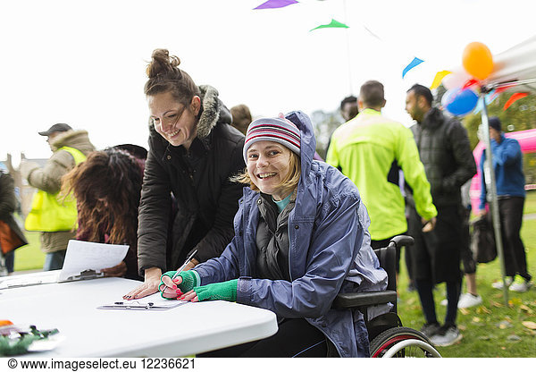 Portrait smiling woman in wheelchair checking in for charity race in park