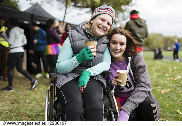 Portrait smiling woman in wheelchair with friend  drinking water at charity race in park