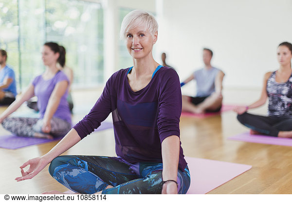 Portrait smiling woman sitting in lotus position in yoga class