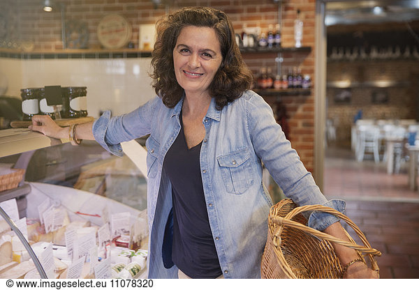 Portrait smiling woman with basket leaning on cheese display case in market