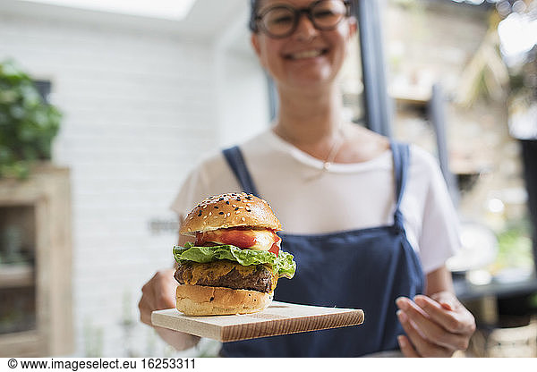 Portrait smiling woman with cheeseburger on cutting board