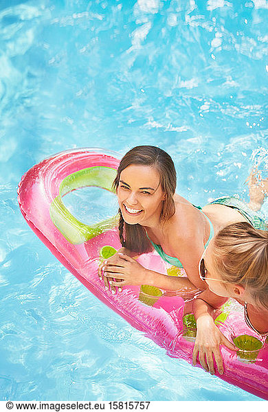 Portrait smiling women friends floating on pool raft in summer swimming pool