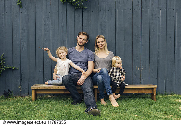 Portrait von glücklichen Eltern und Kindern  die auf Sitzen gegen den Zaun im Hof sitzen.