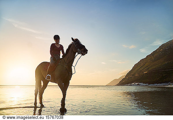 Portrait young woman horseback riding on tranquil sunset ocean beach