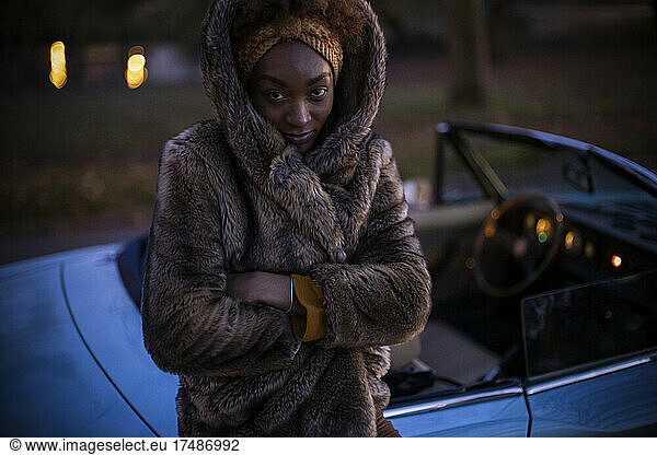 Portrait young woman in fur coat outside convertible at night