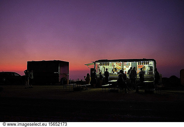 Portugal  Algarve  Purple sky over silhouettes of people relaxing at concession stand in Cape Saint Vincent at dawn