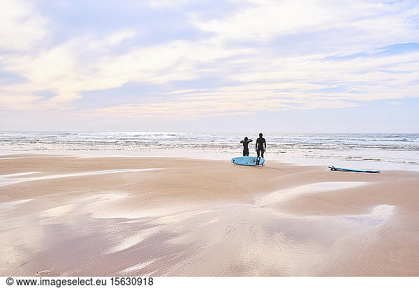 Portugal  Algarve  Silhouetten zweier Surfer  die am Strand von Cordoama stehen