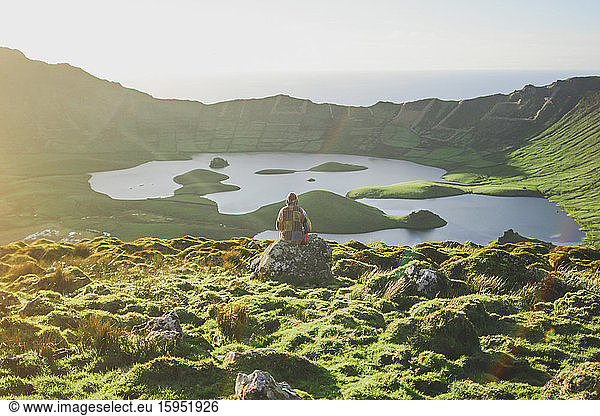 Portugal  Azoren  Junge Frau sitzt auf einem Felsblock und bewundert die vulkanische Landschaft von Caldeirao