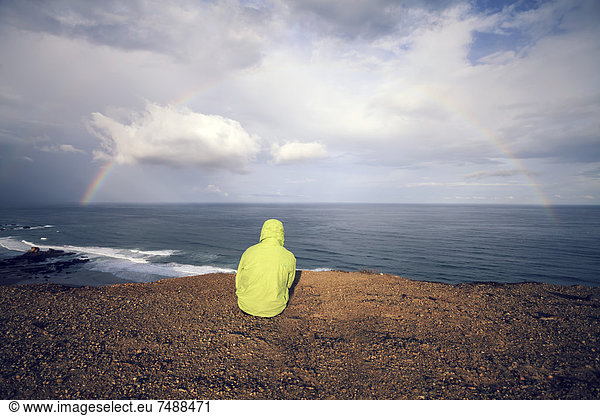 Portugal  Junger Mann sitzend in Praia do Castelejo