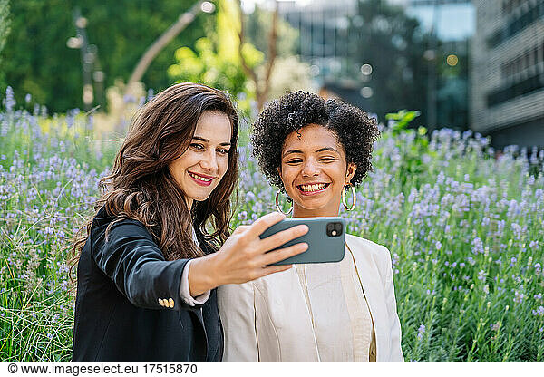 Positive young diverse women taking selfie on smartphone in city park