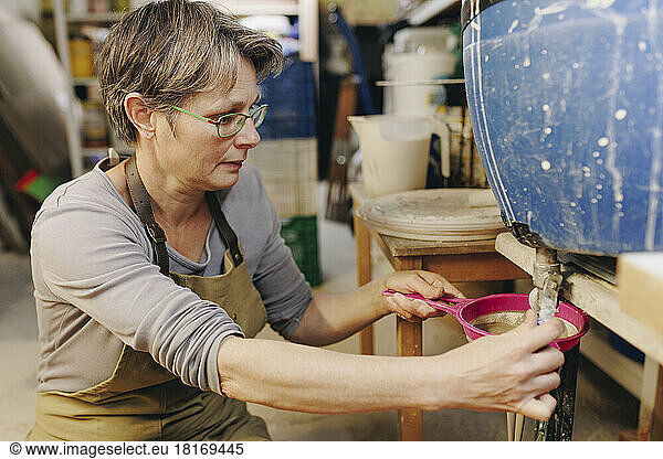 Potter straining clay with colander at ceramics workshop