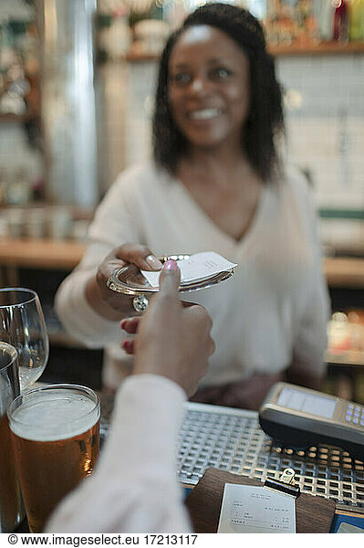 POV customer receiving bill from female bartender in pub