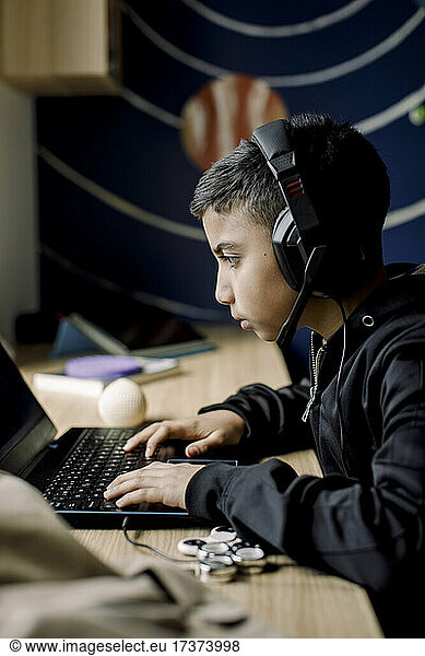 Pre-adolescent boy playing game on laptop in bedroom