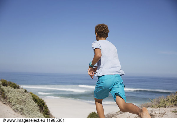 Pre-adolescent boy running on sunny summer ocean beach