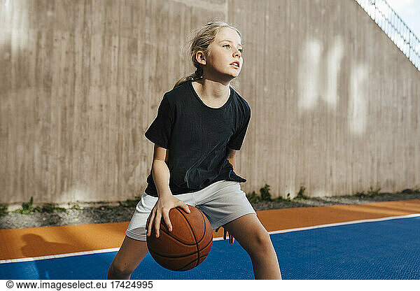 Pre-adolescent girl looking away while playing basketball at sports court