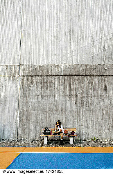 Pre-adolescent girl sitting on bench against wall