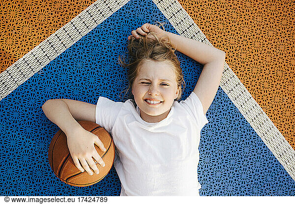 Pre-adolescent girl with basketball winking eye while lying on court