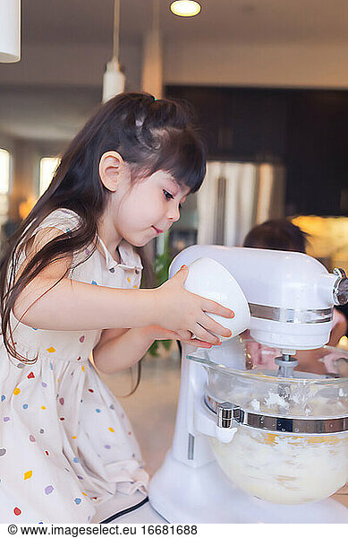 Pre-schooler baking with her family  adding ingredients to the mixer.