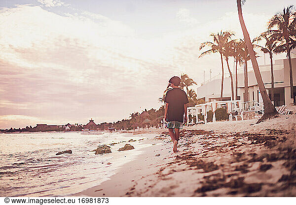 Pre teen boy walking on a tropical beach at sunset.