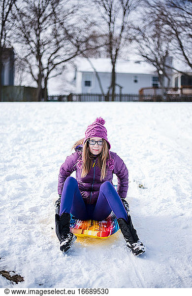 pre teen sitting on sled in the snow in winter