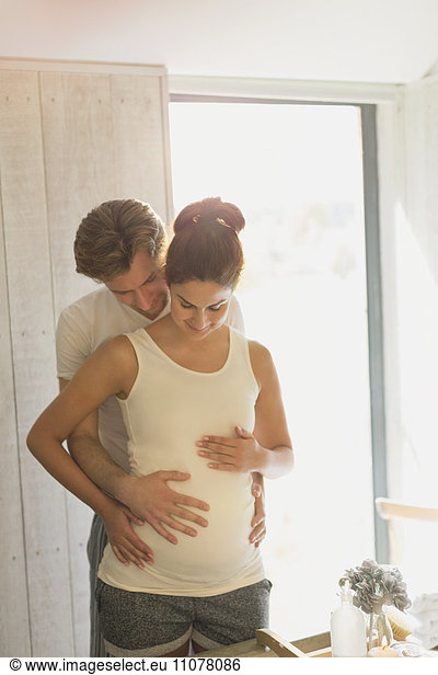 Pregnant couple holding stomach in sunny bathroom