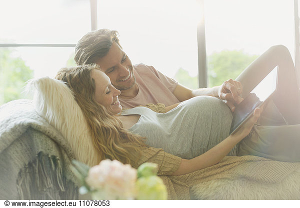 Pregnant couple laying relaxing using digital tablet