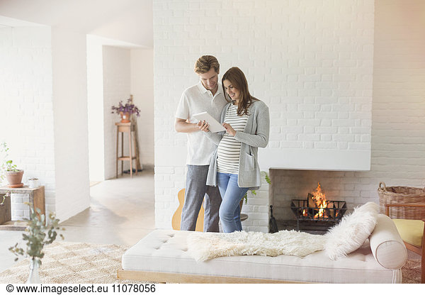Pregnant couple using digital tablet near fireplace
