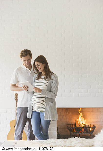 Pregnant couple using digital tablet near fireplace