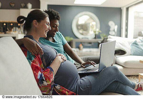 Pregnant couple using laptop on living room sofa