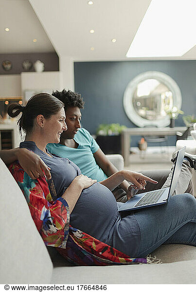 Pregnant couple with laptop on living room sofa
