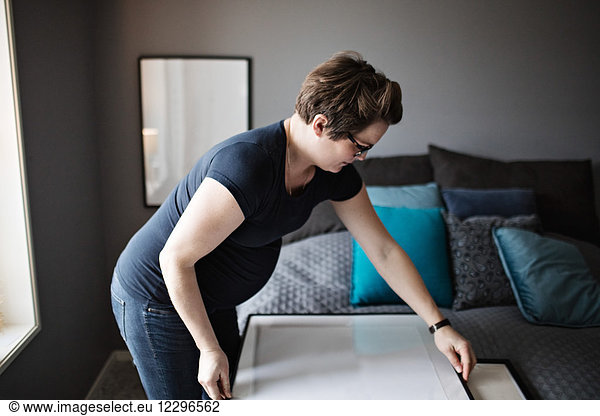 Pregnant mid adult woman arranging paintings on bed by gray wall in bedroom at home