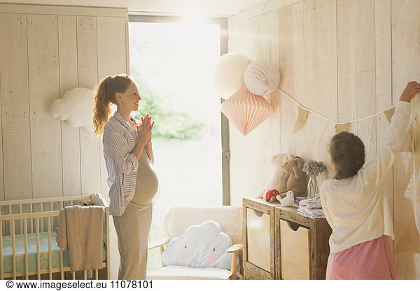 Pregnant mother and daughter decorating sunny nursery