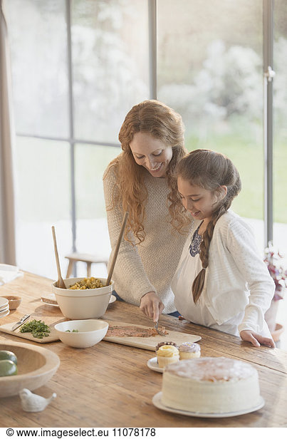 Pregnant mother and daughter preparing food at dining table