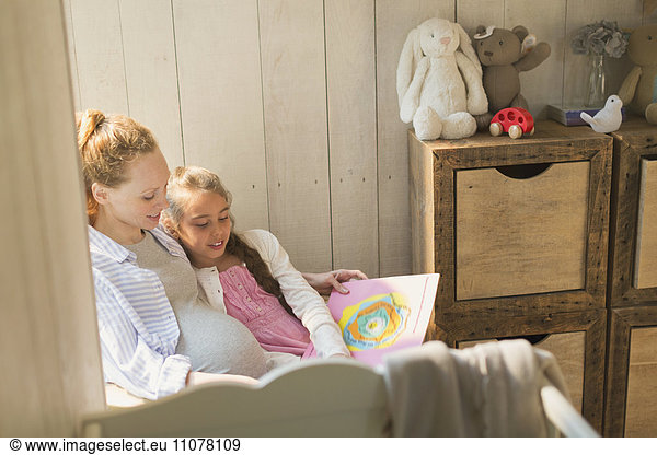 Pregnant mother and daughter reading story book in nursery