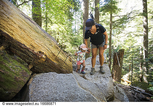 Pregnant mother helps her two year old hiking on rocky terrain.
