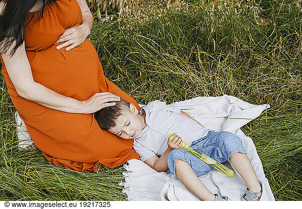 Pregnant mother stroking sleeping son on grass