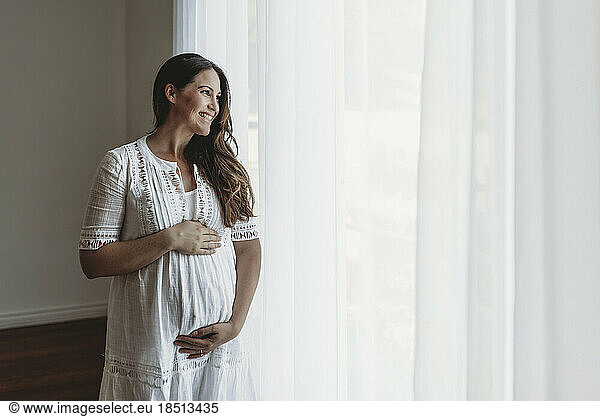 Pregnant smiling mother in white looking out of studio window