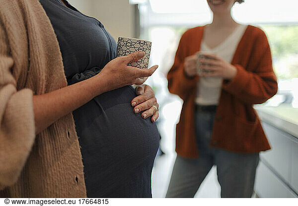 Pregnant woman and friend drinking tea in kitchen