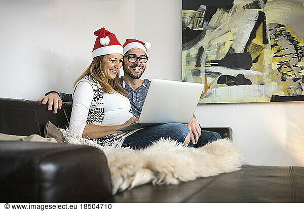 Pregnant woman and husband wearing Santa hat and shopping on laptop  Munich  Germany
