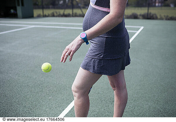 Pregnant woman bouncing tennis ball on tennis court