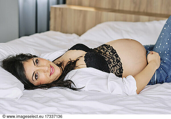 Pregnant woman contemplating while lying on bed at home