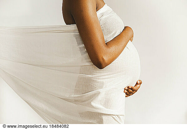 Pregnant woman covered in white sheet in front of wall