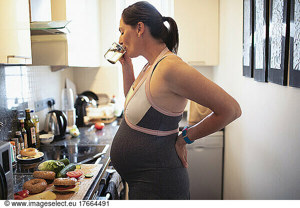 Pregnant woman drinking and eating in kitchen