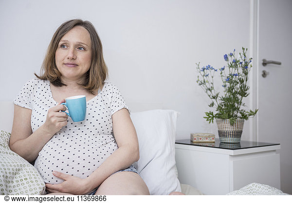 Pregnant woman drinking cup of coffee in bed