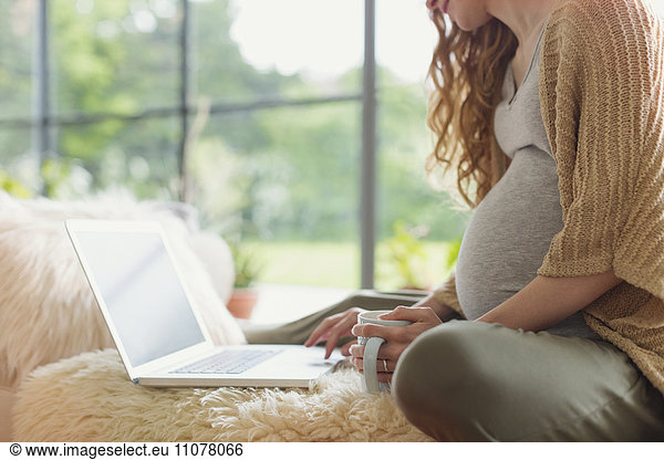 Pregnant woman drinking tea and using laptop