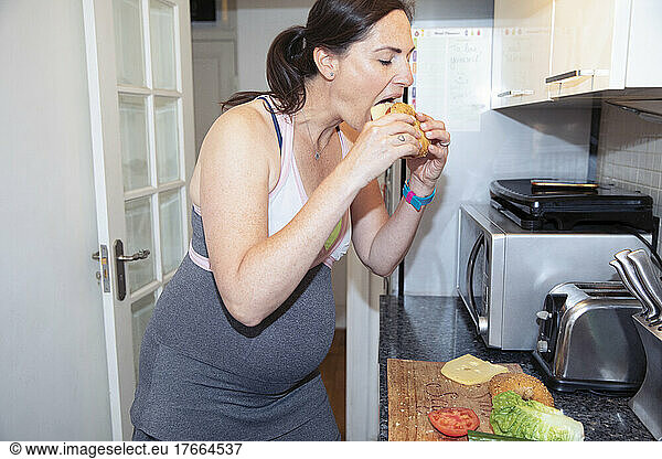 Pregnant woman eating sandwich in kitchen