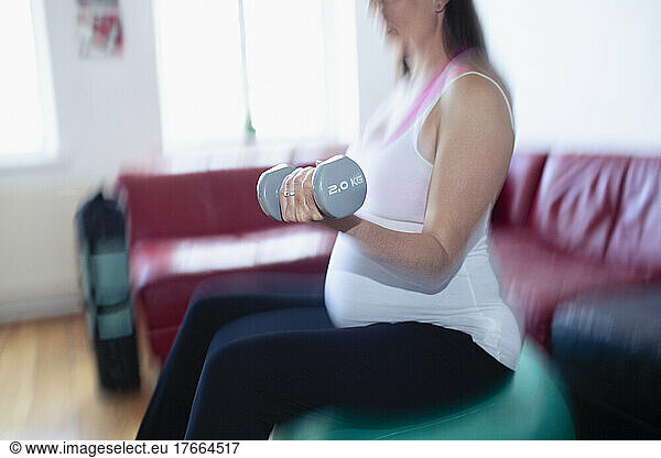 Pregnant woman exercising with dumbbells on fitness ball at home