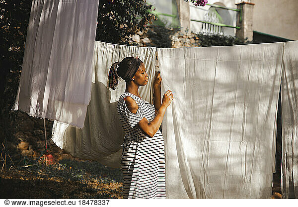 Pregnant woman hanging white sheet at backyard