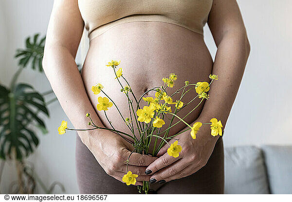 Pregnant woman holding bunch of flowers at home